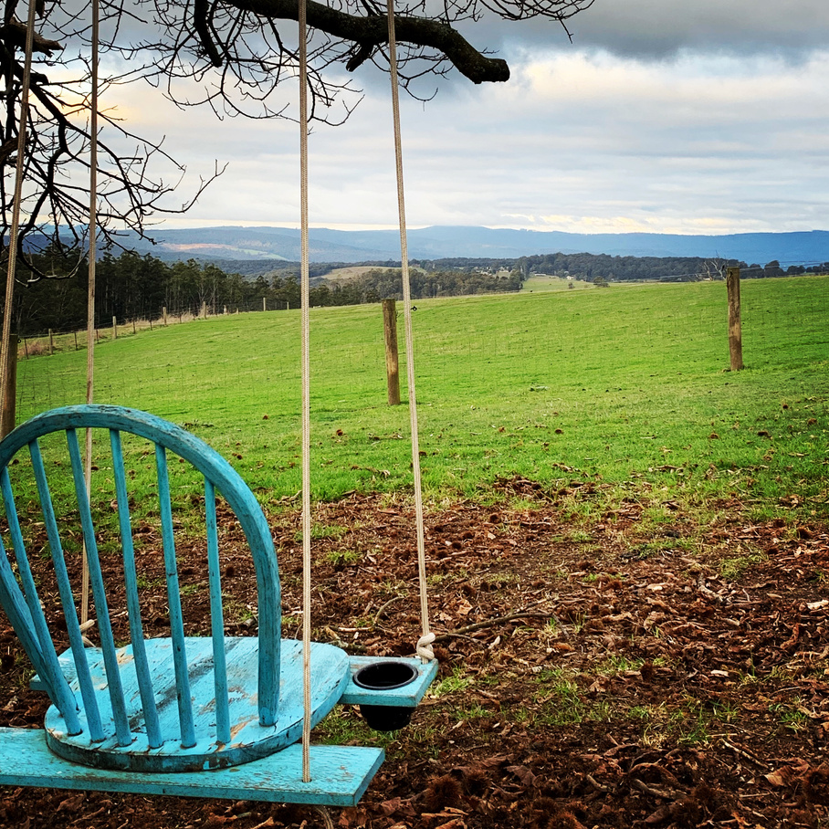 a blue wooden swing sitting in the middle of a grassy field