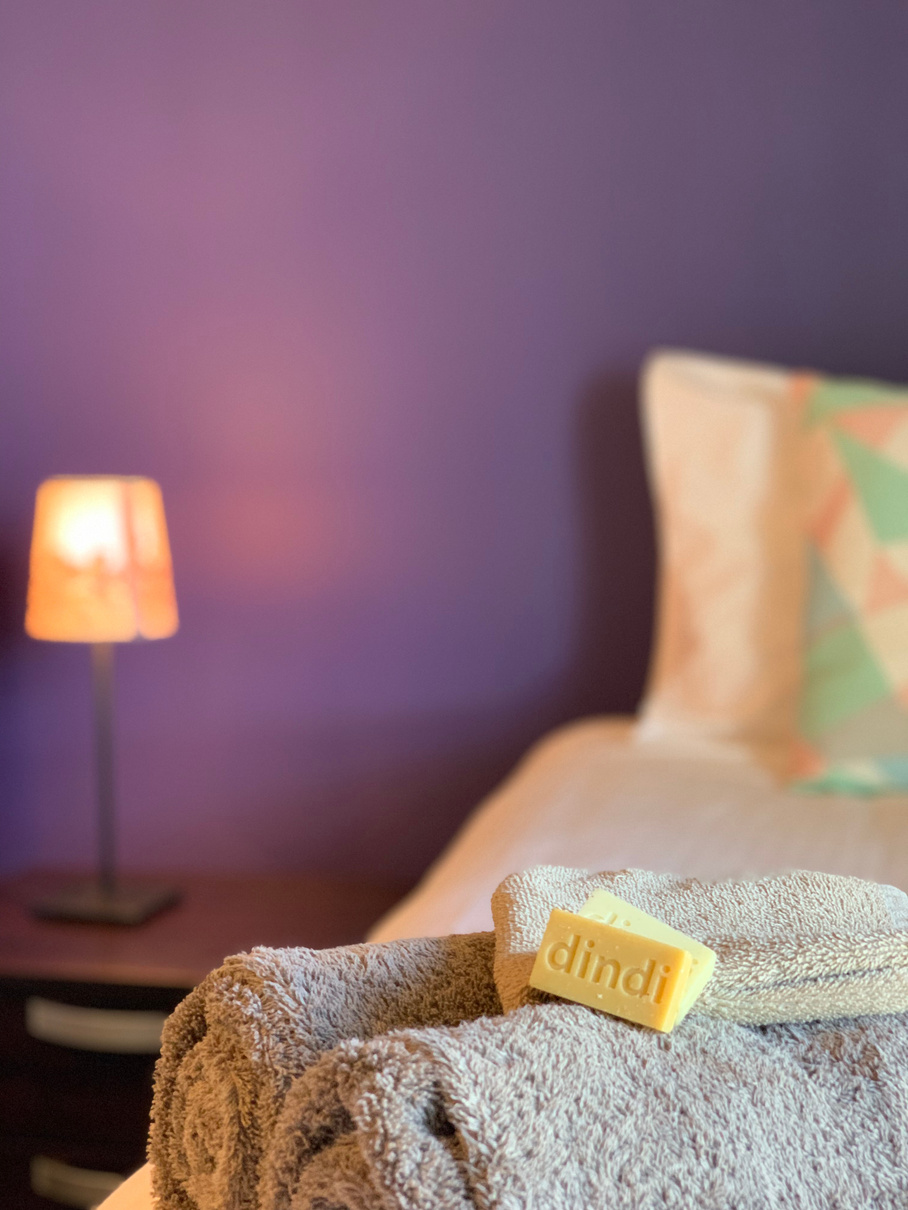 a towel and soap on a bed in front of a purple wall